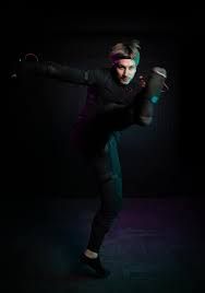 Performer in a motion capture suit mid-kick against a dark background